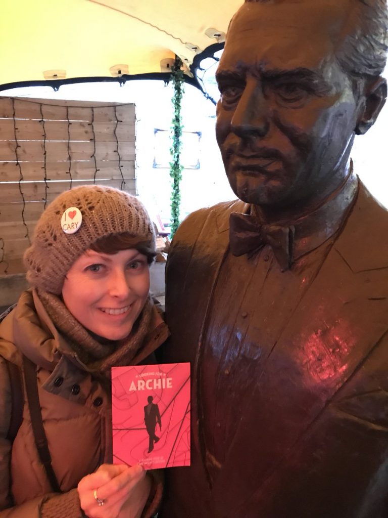 Participant holding the Looking For Archie Walking Tour map up next to the Cary Grant statue