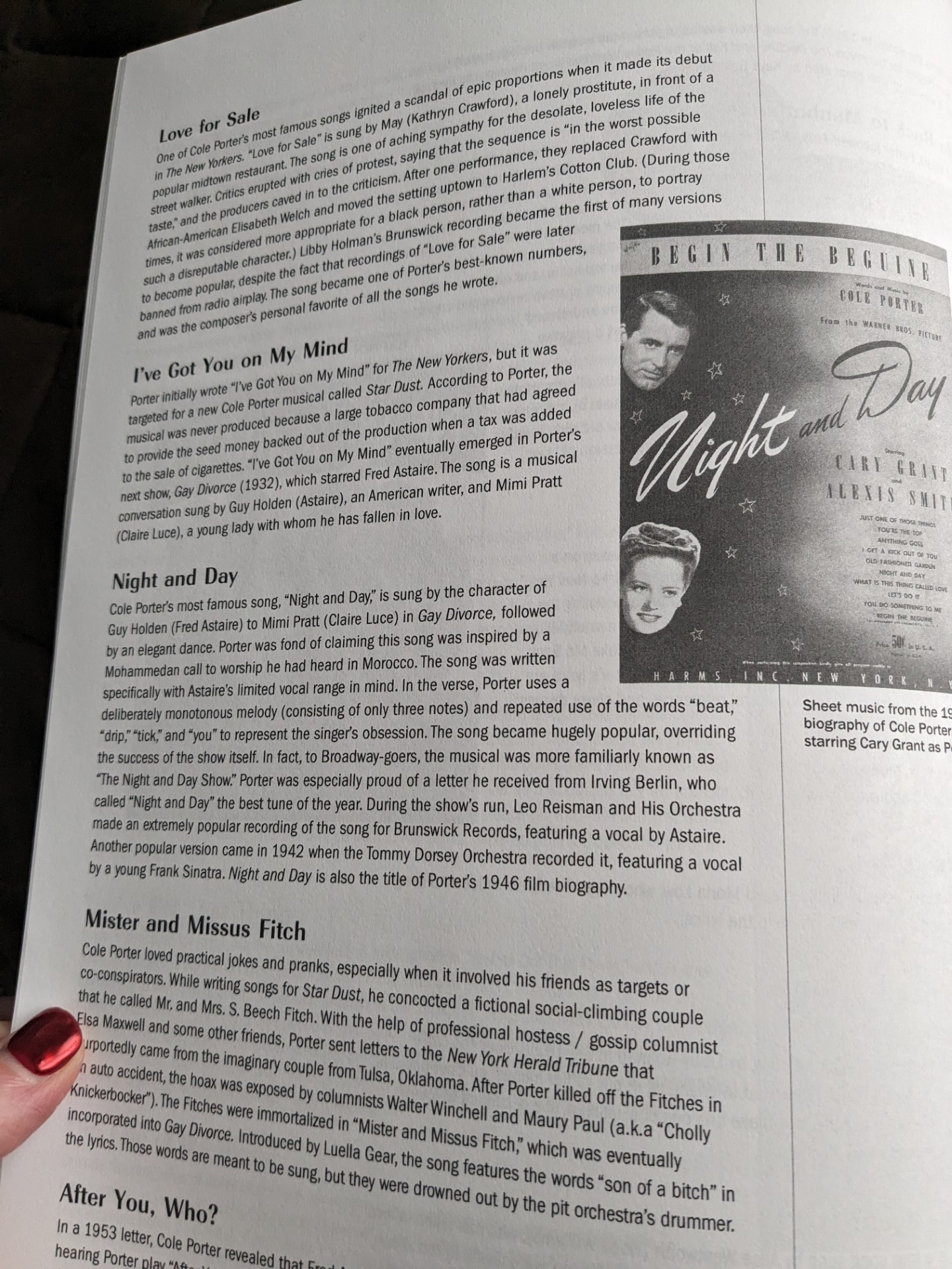 A woman's red painted thumbnail holds open a page of the Cole Porter Song Collection, featuring a black and white poster of the sheet music of Begin the Beguine from Night and Day with the disembodied heads of Cary Grant and Alexis Smith on a dark star-studded backdrop