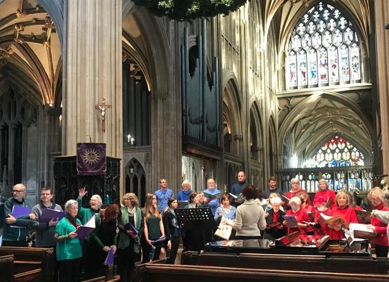 Choristers dressed in green, blue and red singing in front of pews with wonderful stained glass arched windows behind in a gothic-style church with a pulpit and vaulted ceilings